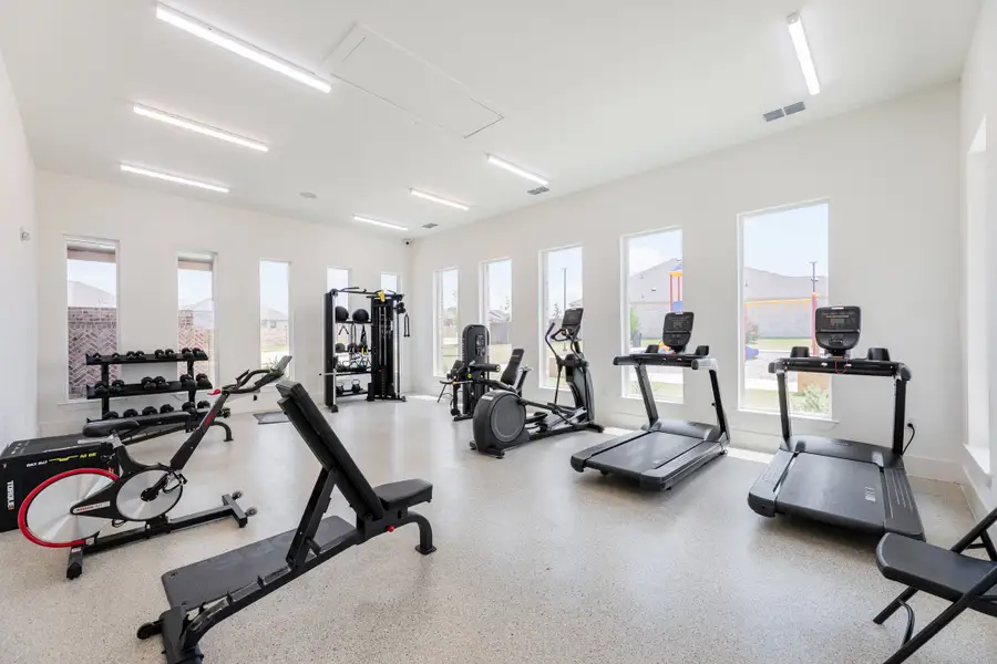 Fitness room with treadmills, elliptical, weight bench, and dumbbell rack along bright white walls with large windows