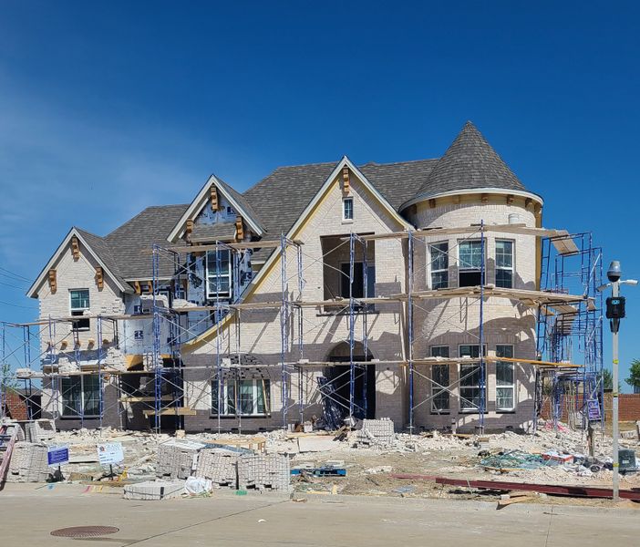 A grand brick home under construction at Silverleaf Estates in Frisco by Grand Homes, featuring scaffolding and large windows.