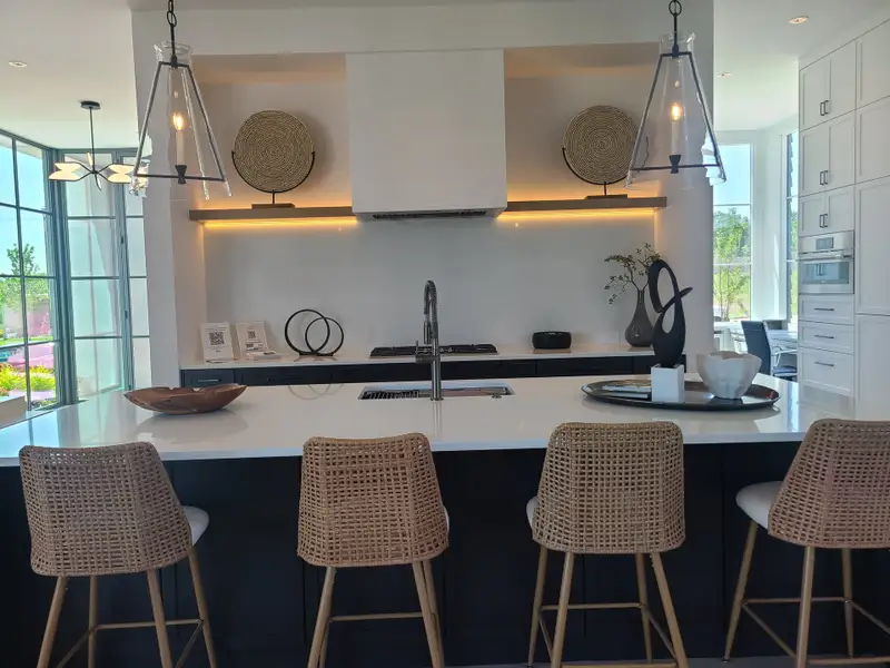 A modern kitchen with sleek lighting, woven barstools, and elegant décor accents. Bright and inviting space for culinary creativity.