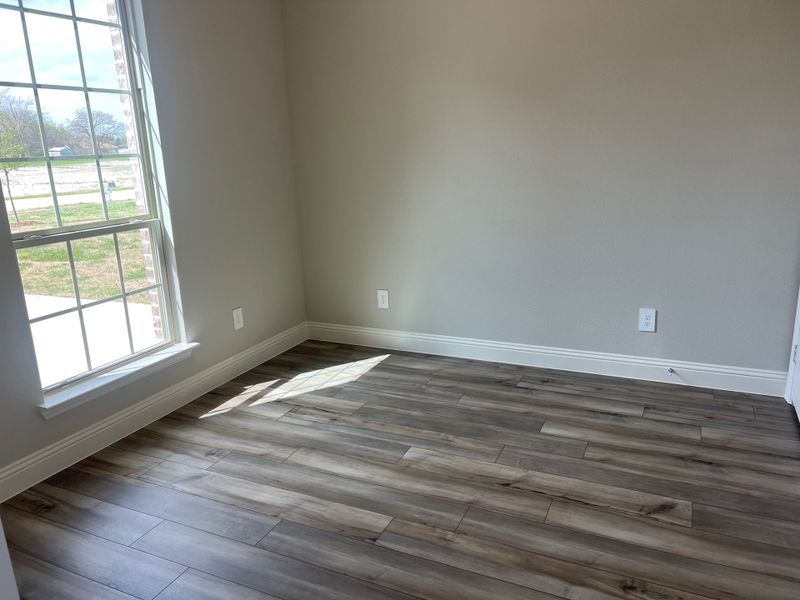 A bright room featuring wood-look flooring and a large window with abundant natural light.