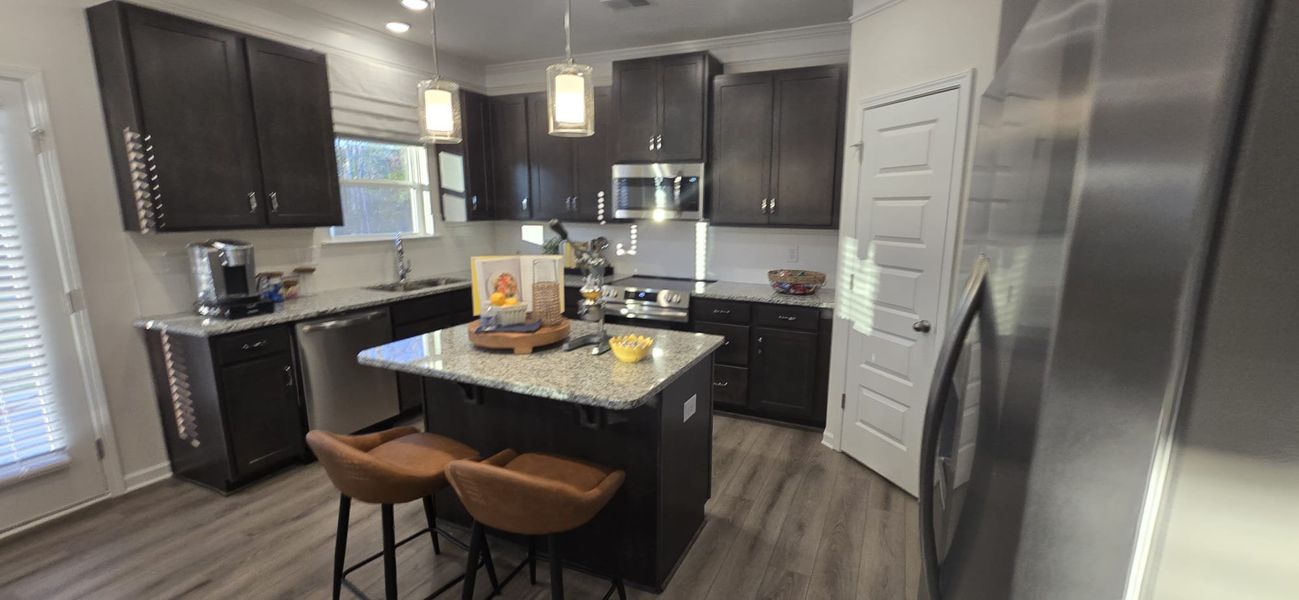 A sleek kitchen with dark cabinets, granite countertops, and modern lighting, featuring a cozy island with seating.