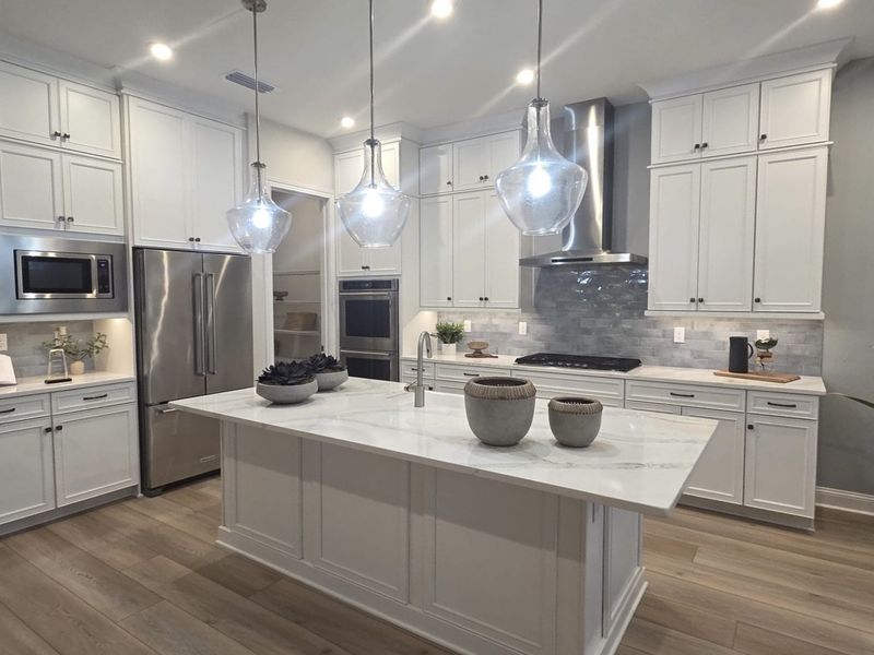 A modern kitchen with white cabinetry, a marble island, pendant lights, and stainless steel appliances. A modern kitchen with white cabinetry, a marble island, pendant lights, and stainless steel appliances.