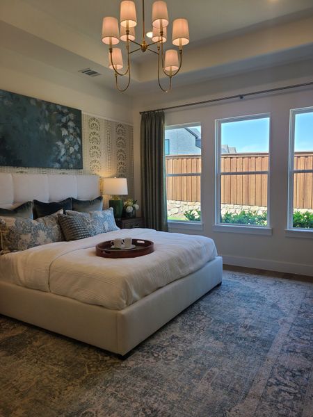 A cozy bedroom with elegant wallpaper, a large white bed, stylish chandelier, and natural light from three windows.