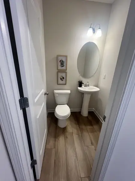 A cozy bathroom with wood-look flooring, pedestal sink, round mirror, and soft lighting.