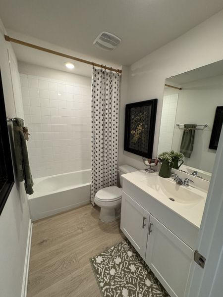 A cozy bathroom with patterned shower curtain, white vanity, and wooden floor, creating a warm and inviting atmosphere.