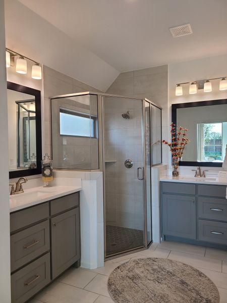 A chic bathroom featuring a glass shower, dual gray vanities, and warm lighting for a modern touch. A chic bathroom featuring a glass shower, dual gray vanities, and warm lighting for a modern touch.