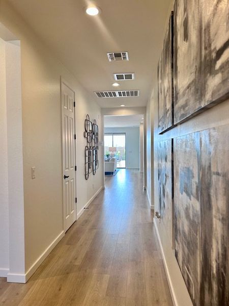 Bright hallway with elegant wood flooring, contemporary artwork, and recessed lighting, leading to a sunny room with a view.