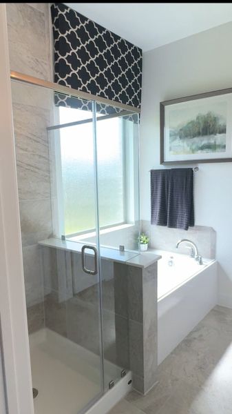 A modern bathroom with a glass shower, tiled bathtub, and elegant decor, featuring a stylish window treatment. A modern bathroom with a glass shower, tiled bathtub, and elegant decor, featuring a stylish window treatment.