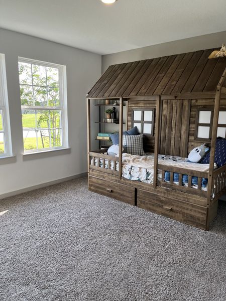 A cozy kids' bedroom with a charming wooden bunk bed designed as a playhouse, carpeted floor, and bright windows.