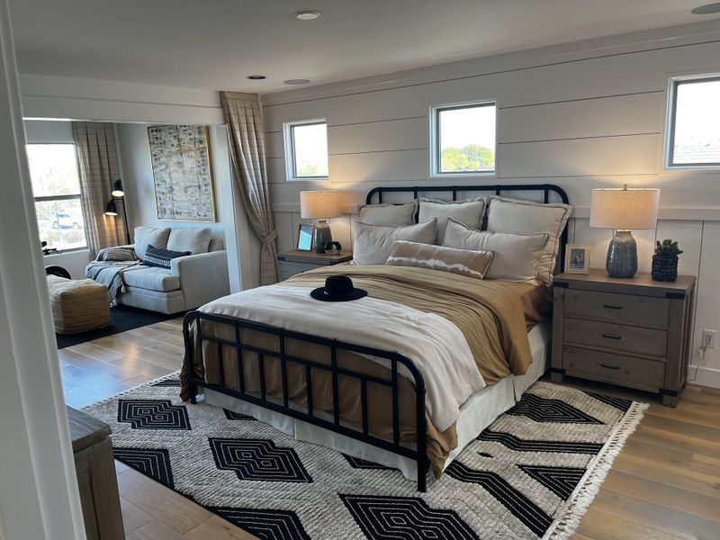 Cozy bedroom with a black metal bed frame, warm-toned bedding, wooden nightstands, and an attached sitting area.