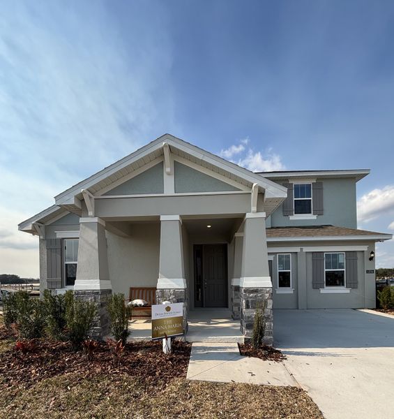 A welcoming two-story home with a charming front porch, neutral exterior tones, and stone accents in Crossroads at Kelly Park by Dream Finders Homes (Apopka, FL).