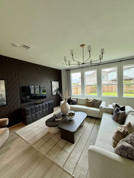 A modern living room with a chic chandelier, dark feature wall, and large windows, featuring plush seating and a stylish coffee table.