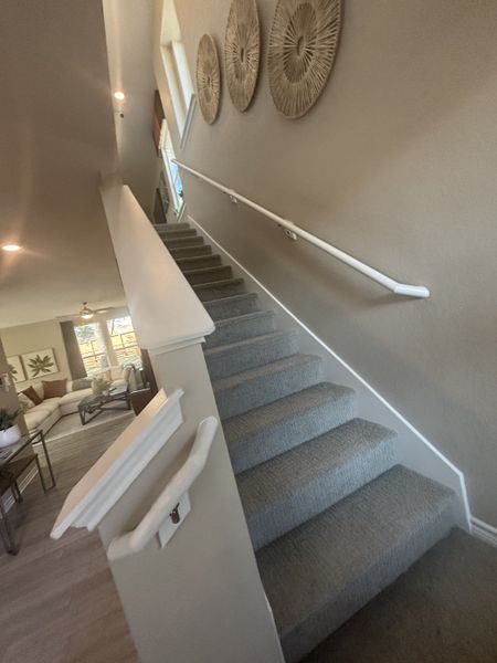 A modern staircase with carpeted steps and decorative wall accents, leading to a cozy, sunlit living area. A modern staircase with carpeted steps and decorative wall accents, leading to a cozy, sunlit living area.