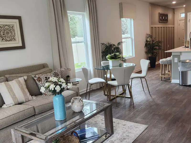 A cozy living area with a neutral sofa, elegant glass dining table, and sleek kitchen bar in an open-plan setting.