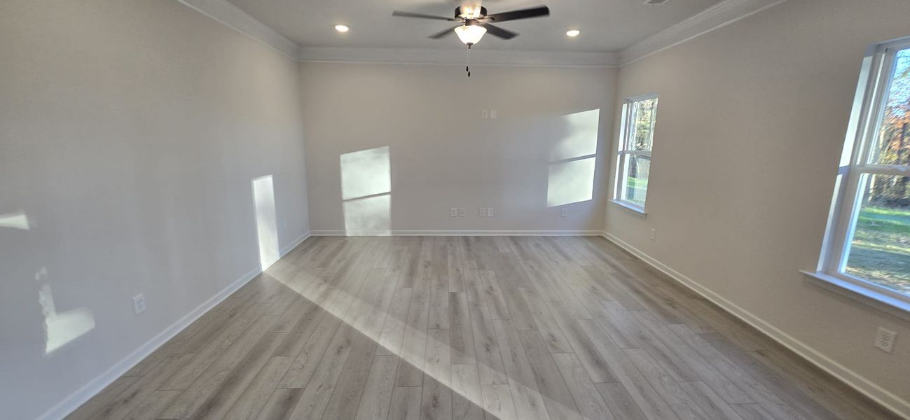 A spacious room with light wood flooring, soft gray walls, and a ceiling fan, featuring large windows for ample natural light.