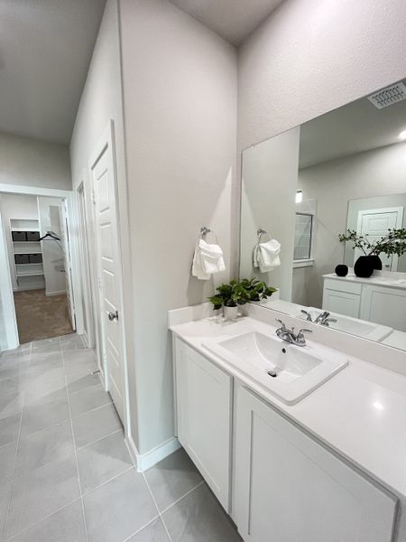 A sleek bathroom with a large mirror, modern white vanity, and elegant gray tiled floor.