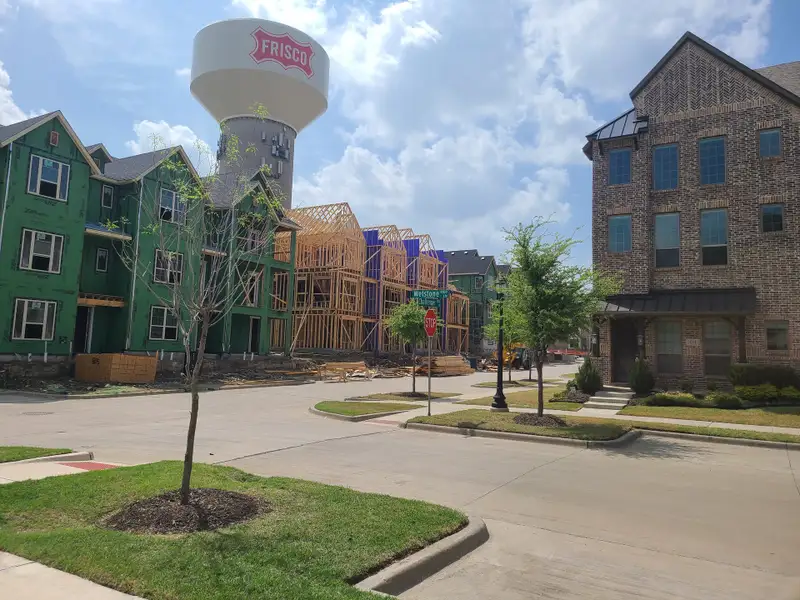 New construction and completed homes in Wade Settlement by Megatel Homes, Frisco, TX, with a prominent water tower nearby.