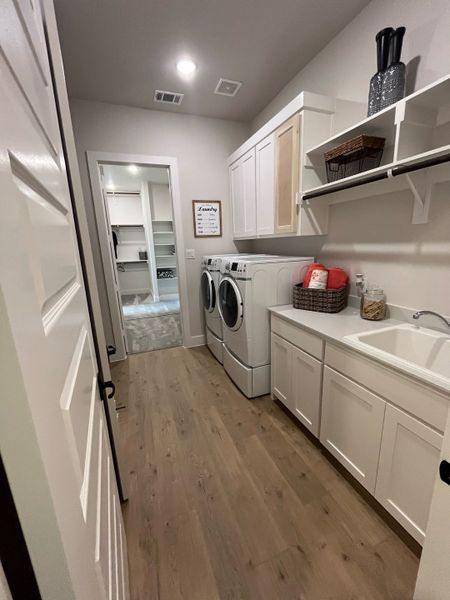 A spacious laundry room with sleek cabinetry, hardwood floors, and modern appliances.