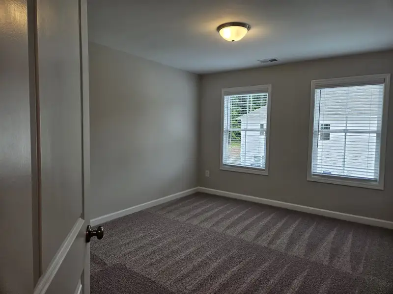 A cozy, carpeted room with soft gray walls and natural light from two windows.