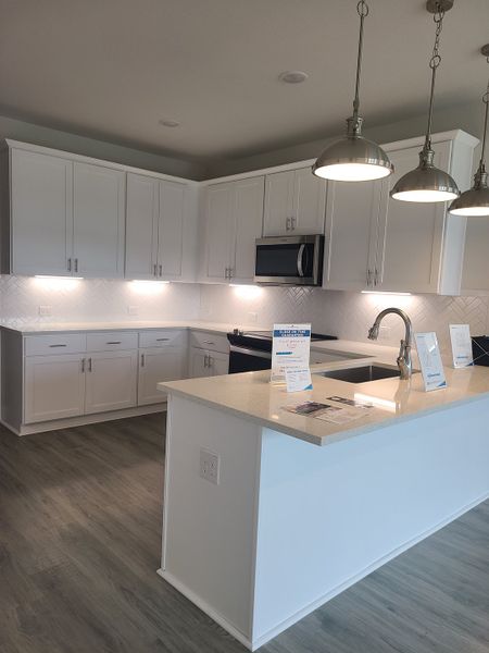 A modern kitchen featuring white cabinetry, a sleek island, herringbone backsplash, and stainless steel appliances. A modern kitchen featuring white cabinetry, a sleek island, herringbone backsplash, and stainless steel appliances.