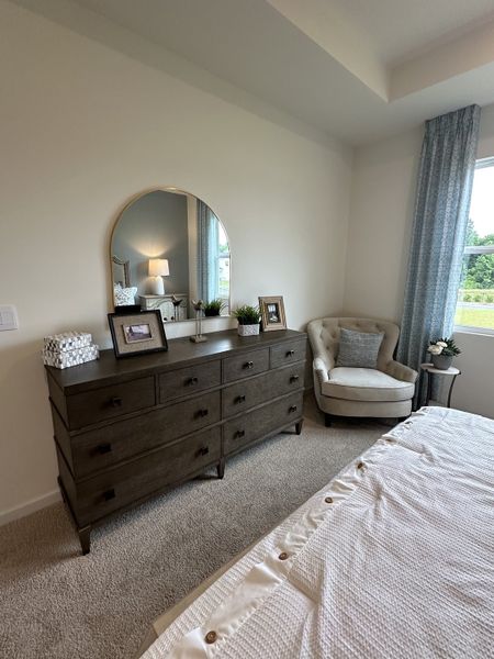 A cozy bedroom with a large wooden dresser, round mirror, soft armchair, and elegant decor.