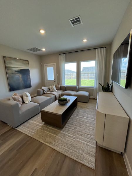 A cozy living room with a large sectional sofa, abstract art, and ample natural light from large windows.
