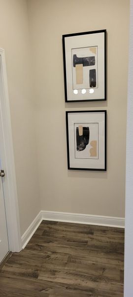 A cozy hallway with abstract framed artwork, warm beige walls, and rich wooden flooring.