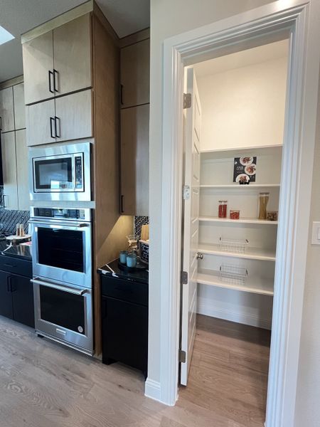 A modern kitchen with sleek appliances, wooden cabinets, and a convenient pantry with white shelving. A modern kitchen with sleek appliances, wooden cabinets, and a convenient pantry with white shelving.