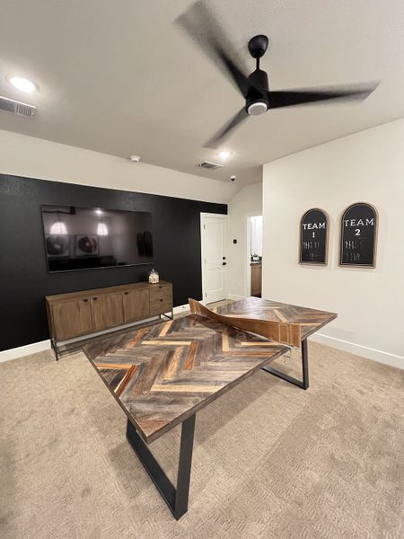 A trendy game room with a large TV, sleek fan, and stylish chevron-patterned tables.