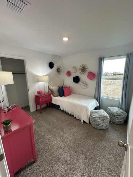 A cozy, bright bedroom with vibrant pink accents, floral wall decor, and soft carpet flooring. Ideal for relaxing.