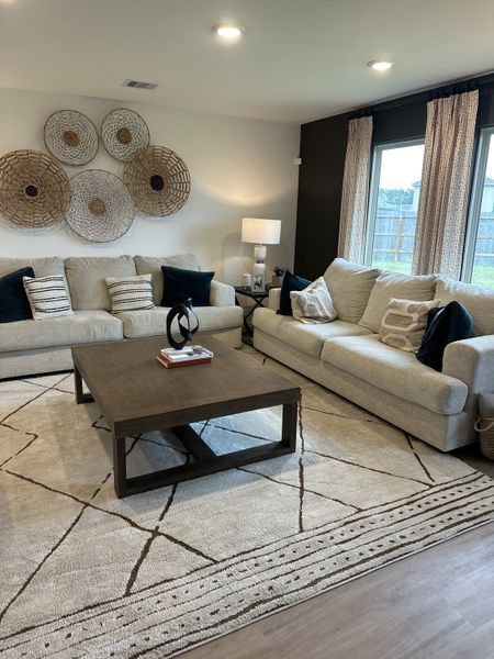 A cozy living room with plush sofas, modern decor, large windows, and an elegant coffee table on a patterned rug. A cozy living room with plush sofas, modern decor, large windows, and an elegant coffee table on a patterned rug.