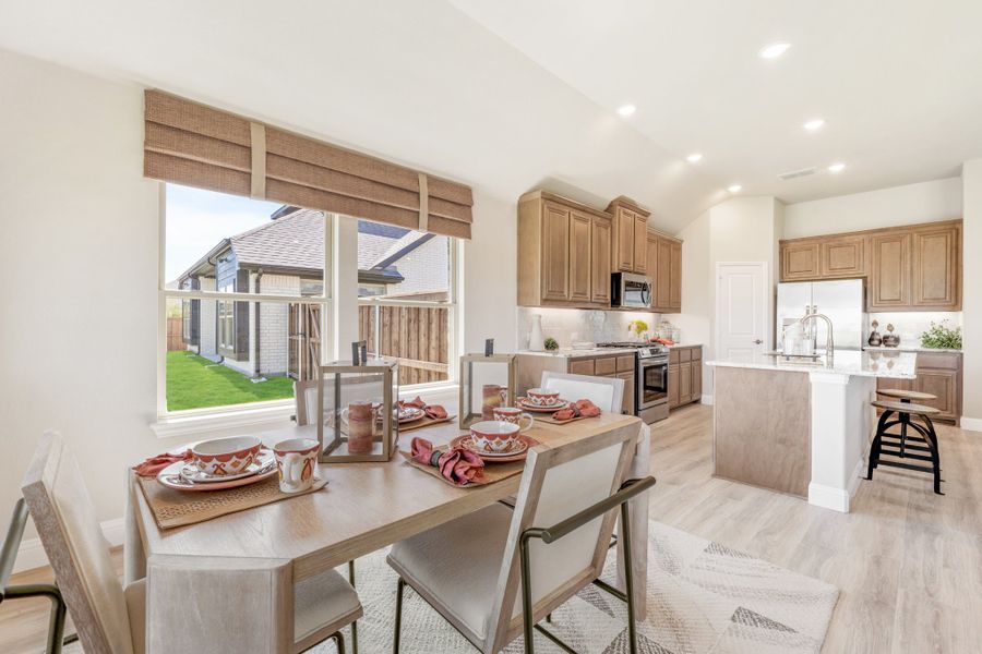 Open dining area with set table flowing into kitchen with brown cabinets, island, and stainless appliances