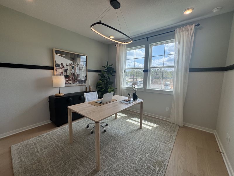 A bright home office featuring a modern desk, stylish artwork, and ample natural light with a large window.