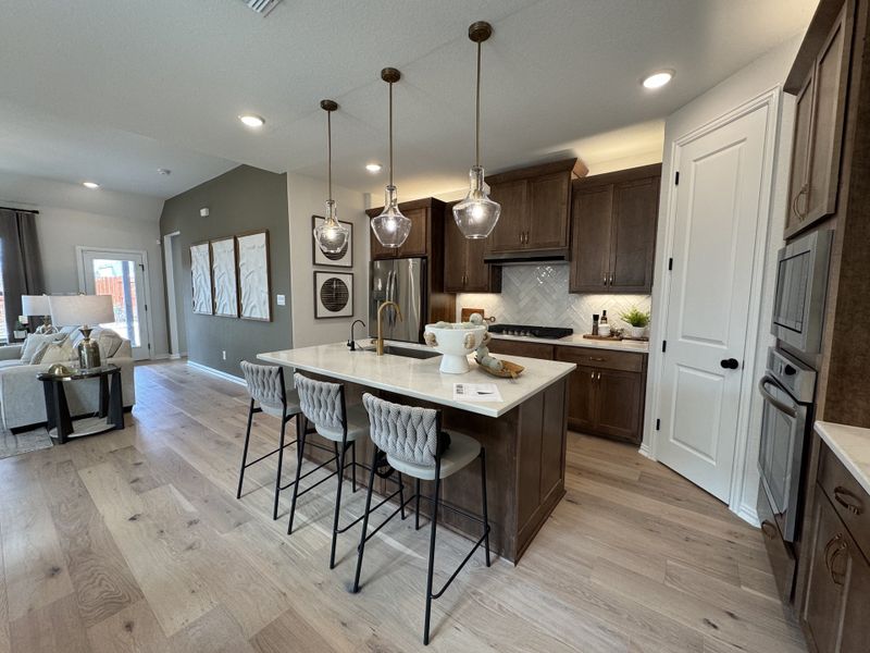 A modern kitchen featuring dark wood cabinetry, stylish pendant lights, and a spacious island with plush seating. A modern kitchen featuring dark wood cabinetry, stylish pendant lights, and a spacious island with plush seating.