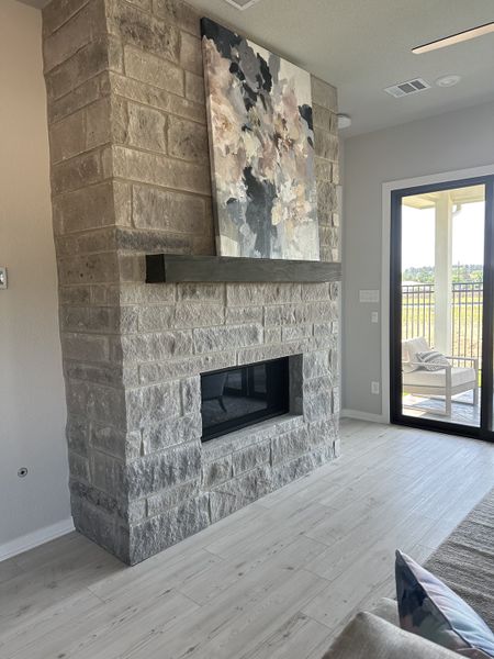 A modern living area with a stone fireplace, abstract artwork, and light wood flooring leading to a patio view.