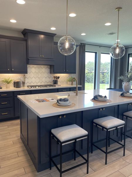 A modern kitchen with navy cabinets, sleek quartz island, pendant lights, and large windows offering lush views. A modern kitchen with navy cabinets, sleek quartz island, pendant lights, and large windows offering lush views.