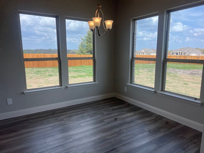 A bright room with large windows, laminate flooring, and a modern chandelier, offering scenic views and natural light.