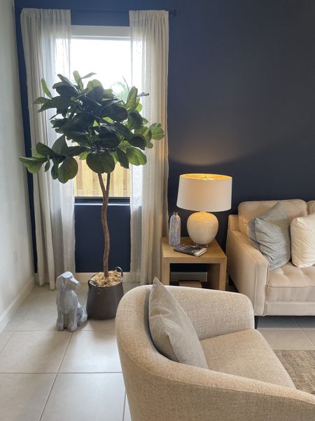 A cozy living room with a beige sofa, chic armchair, indoor plant, and elegant lighting.