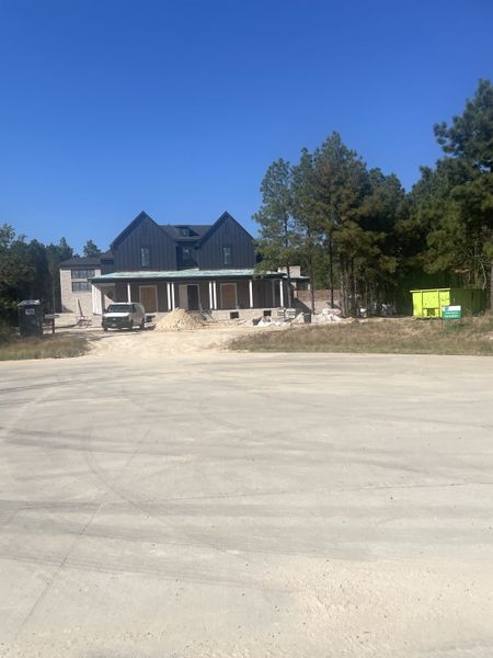 A modern farmhouse under construction surrounded by trees in Tealpointe Lake Estates by Jamestown Estate Homes (Tomball, TX).