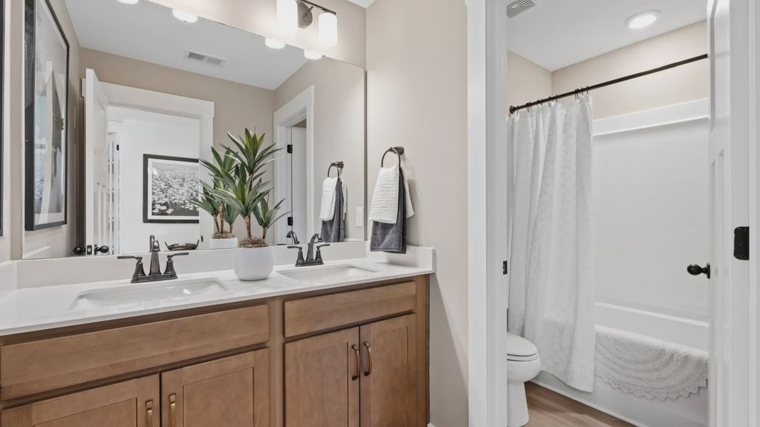 Bathroom with warm wood toned cabinetry with double sink vanity at Fox Hollow by DRB Homes in Spartanburg, SC