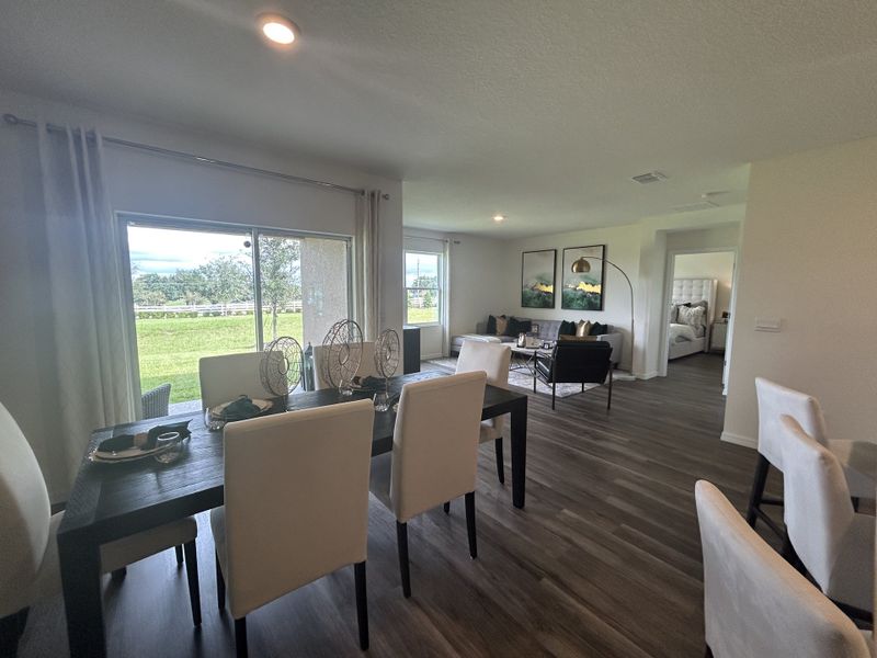 A modern open-concept living and dining area with sleek furniture, wood flooring, and large windows offering scenic views.