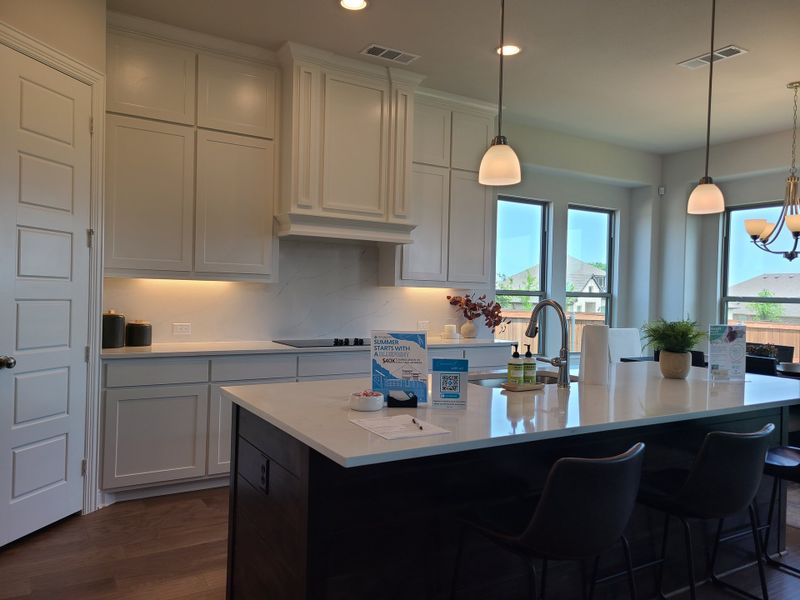 A modern kitchen featuring sleek white cabinets, a spacious island with a sink, and elegant pendant lighting.