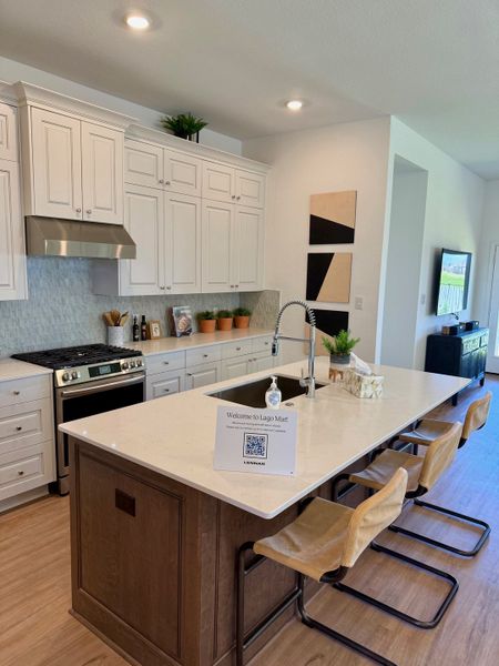 A modern kitchen with sleek white cabinetry, a spacious island with seating, and stainless steel appliances.