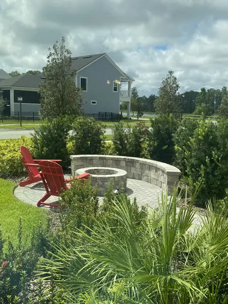 A charming outdoor fire pit with red chairs and lush landscaping in Seven Pines by ICI Homes (Jacksonville, FL).