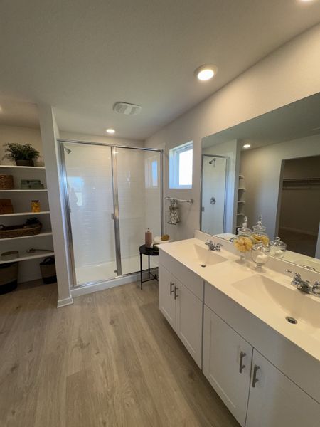 A modern bathroom with dual sinks, glass shower, light wood floors, and open shelving for a clean, fresh look.