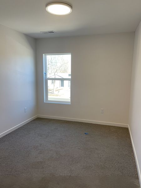 A cozy upstairs bedroom with soft carpeting, natural light, and a neutral design perfect for personalization.