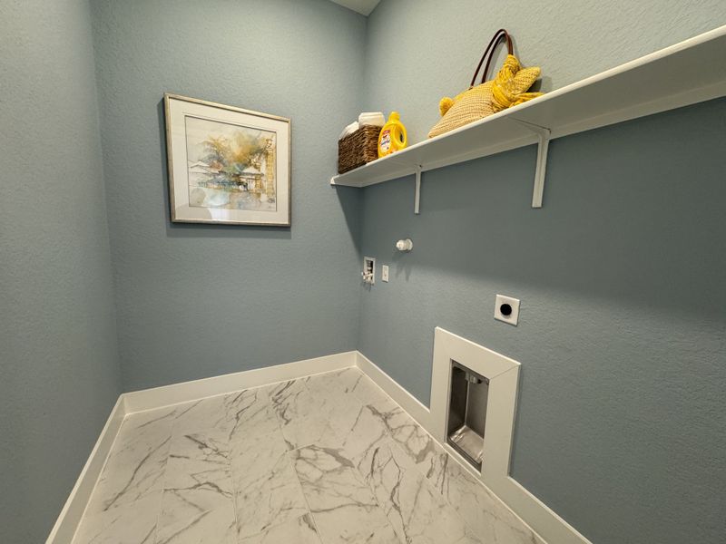 A functional laundry room featuring marble-patterned tile, blue walls, and a convenient storage shelf. A functional laundry room featuring marble-patterned tile, blue walls, and a convenient storage shelf.