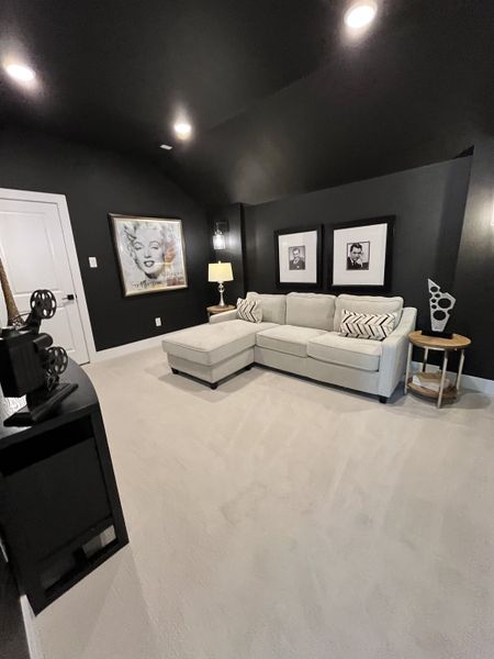 A chic media room with black walls, cozy gray sectional sofa, stylish decor, and contemporary lighting.