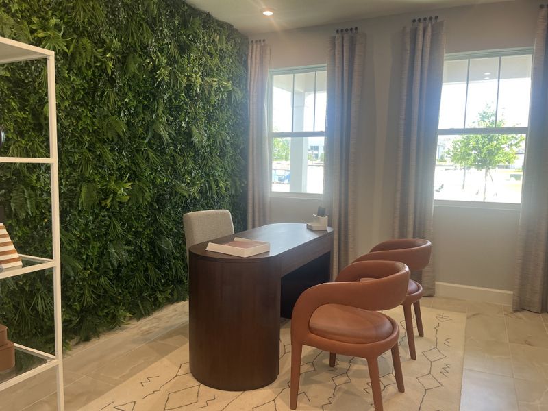 A modern office space featuring a lush green plant wall, wooden desk, and chic leather chairs with ample natural light.