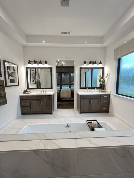 Elegant bathroom with dual sinks, framed mirrors, large bathtub, and chic lighting, offering a luxurious, modern vibe.